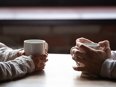 Uplifted Grief two sets of hands holding white mugs across table